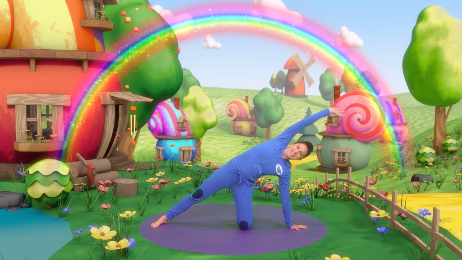 A woman in a blue onesie holds a yoga pose in a colorful fairy tale land in a Cosmic Kids video.